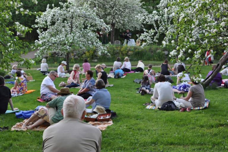 Ihmisiä piknikillä kukkivien omenapuiden alla Voipaalan taidekeskuksen puutarhassa