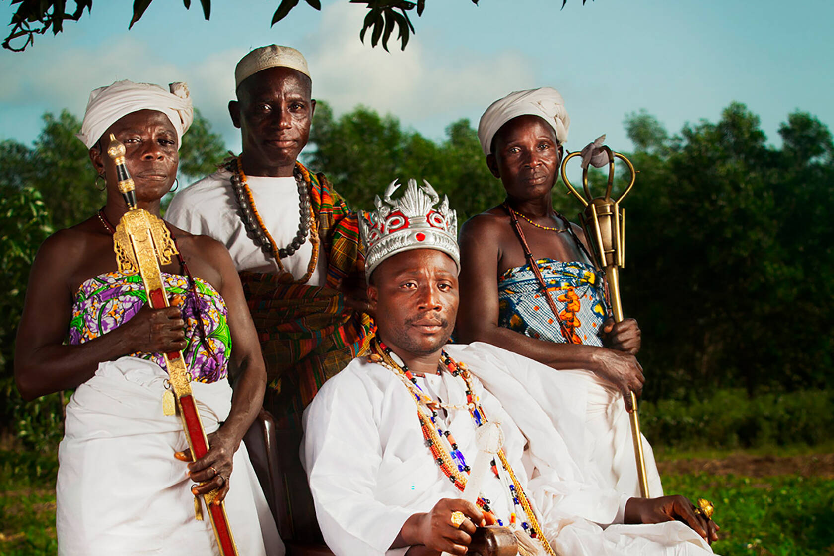 Afrikkalainen kuningas valtaistuimellaan ja kolme ihmistä seisoo hänen takanaan.